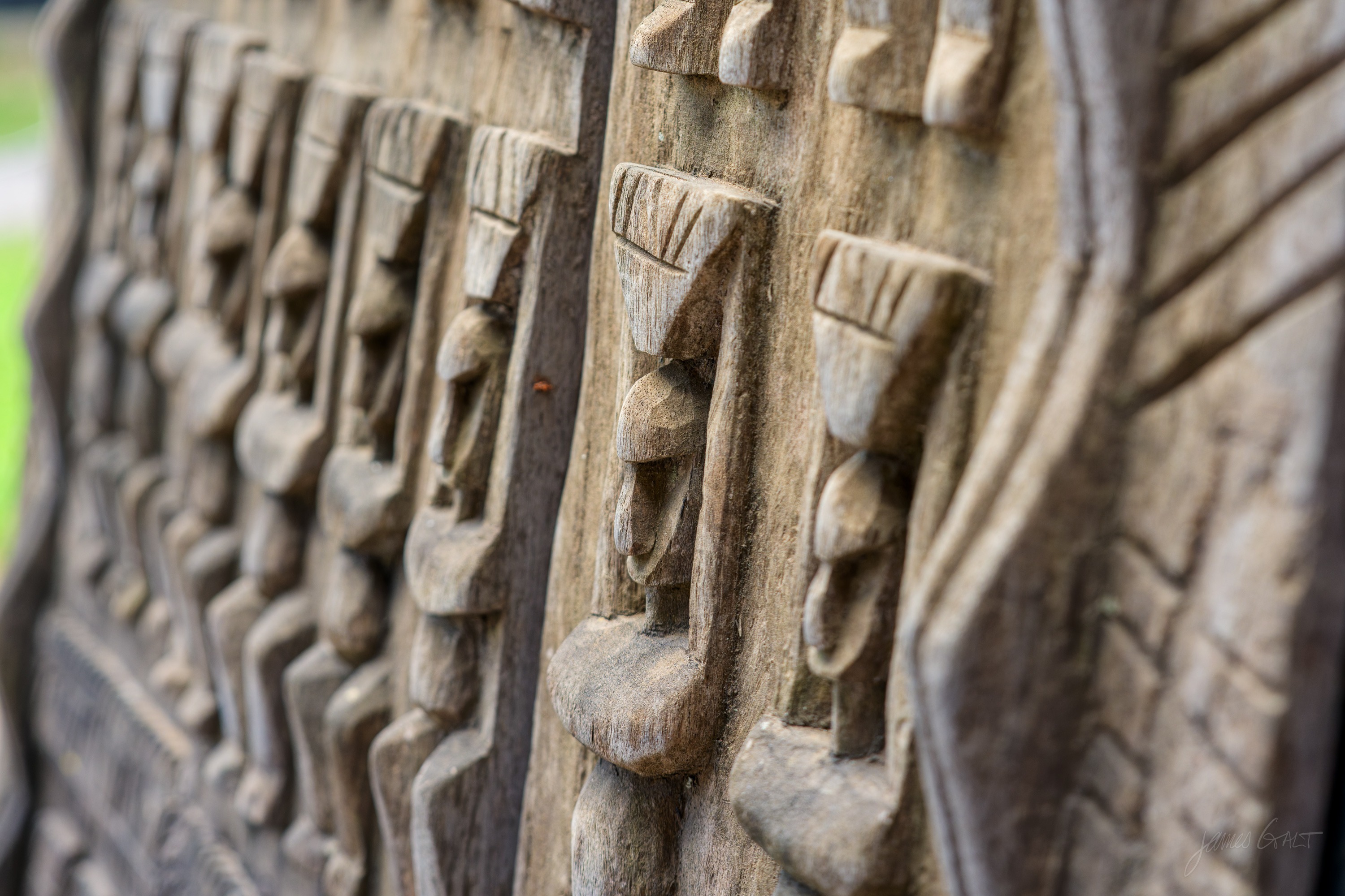 A carved wooden panel in low relief showing a row of stylised standing figures, lit from the side.