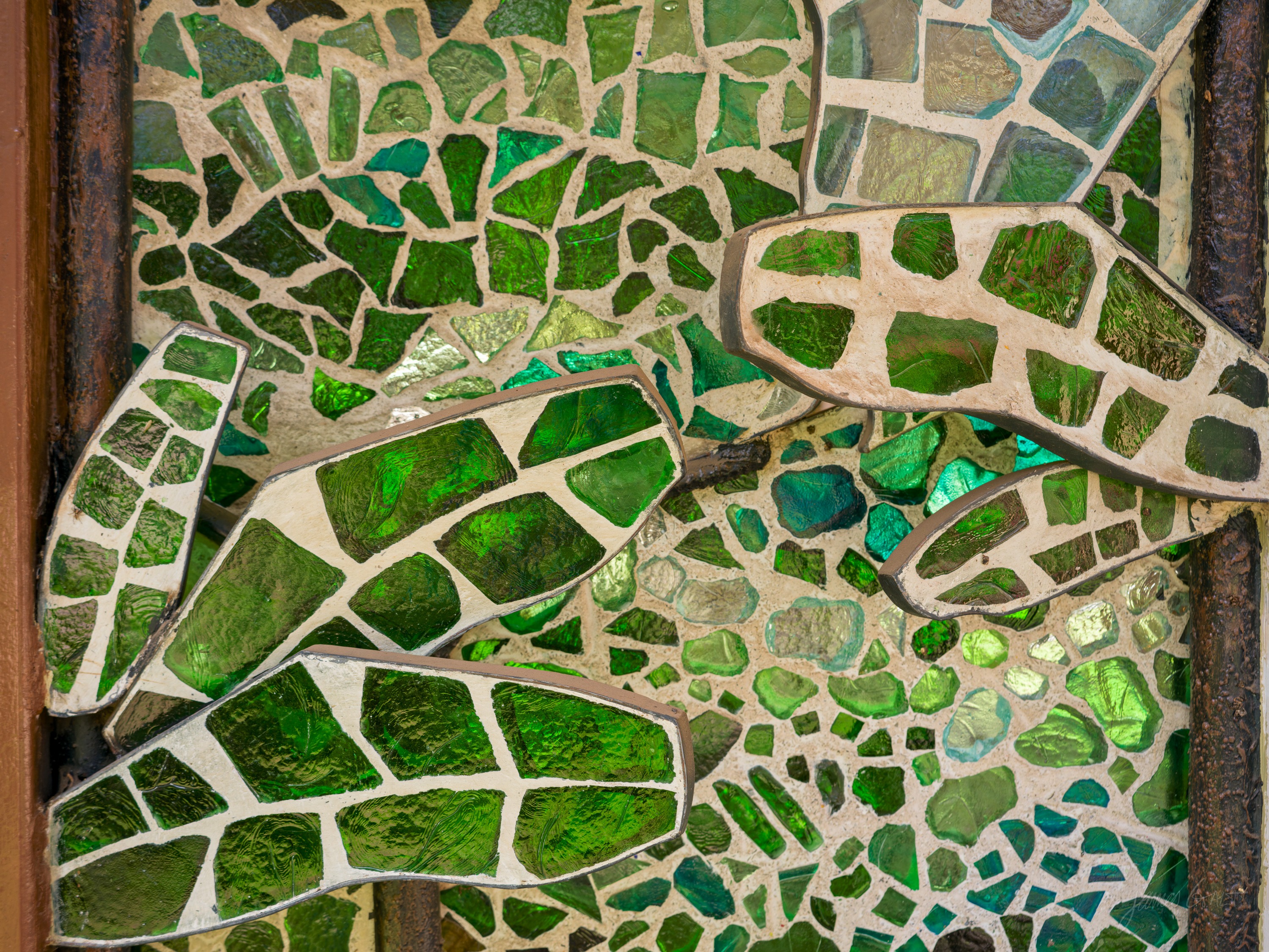 A mosaic of a leaf made from pieces of green and clear glass set in dark grout, with mirrored fragments catching the light.