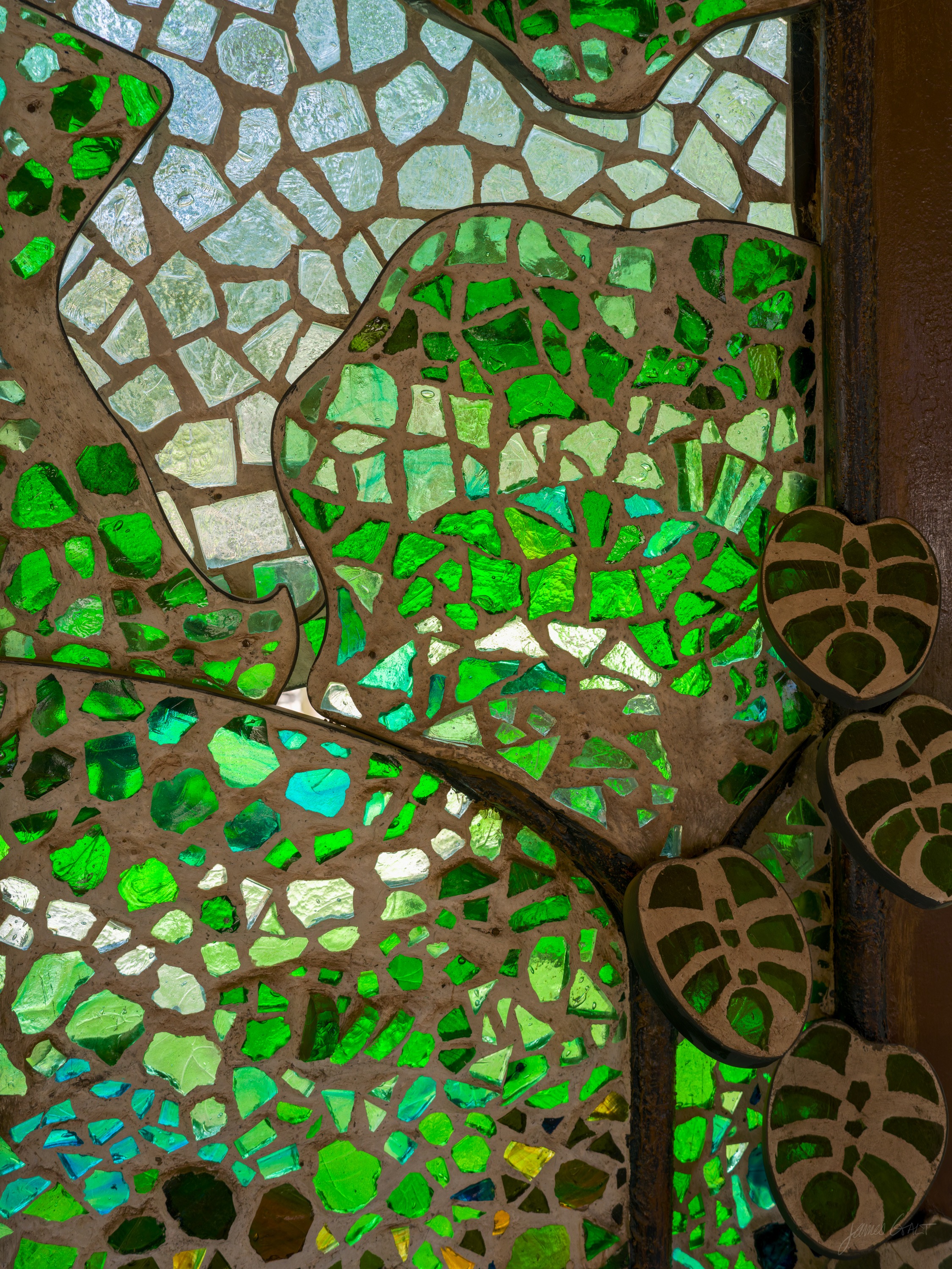 A mosaic panel of a vine and leaves in green glass tiles against a paler glass background, mirror pieces set among them.