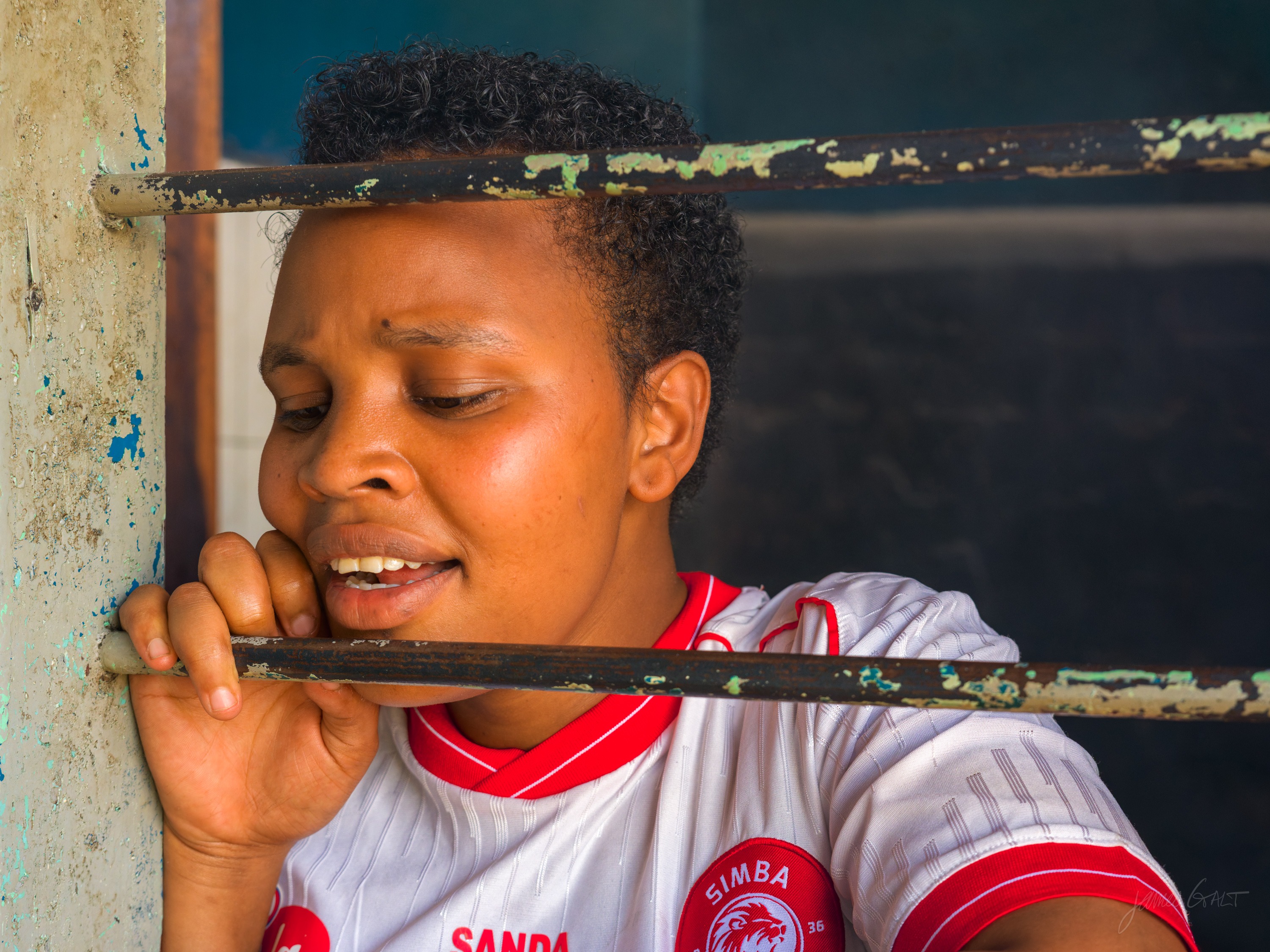 The same woman in colour, in a red and white top, resting by a barred window with her eyes closed.