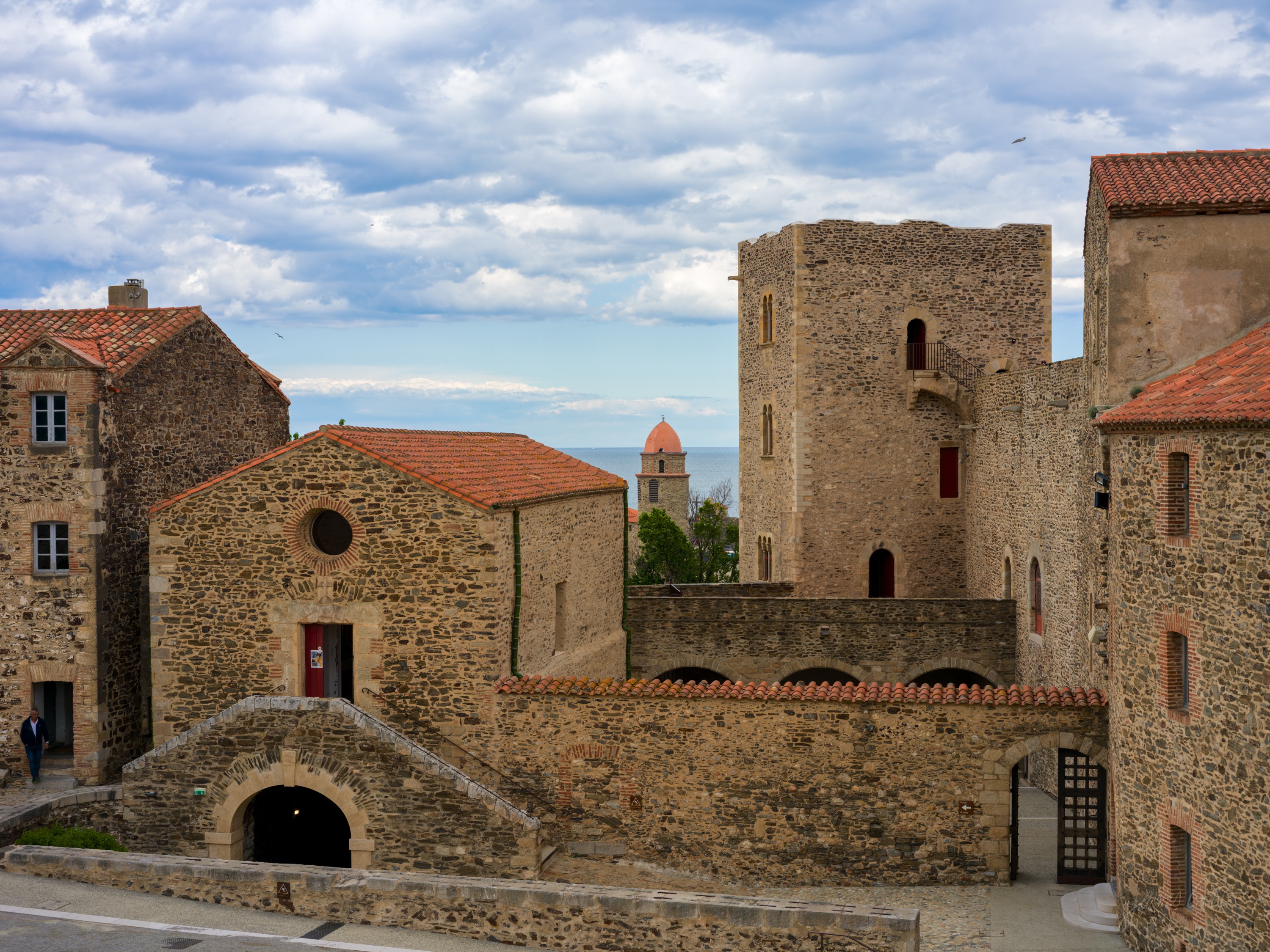 Old stone houses with terracotta roofs clustered below a domed bell tower, the sea just visible between them under a bright sky.