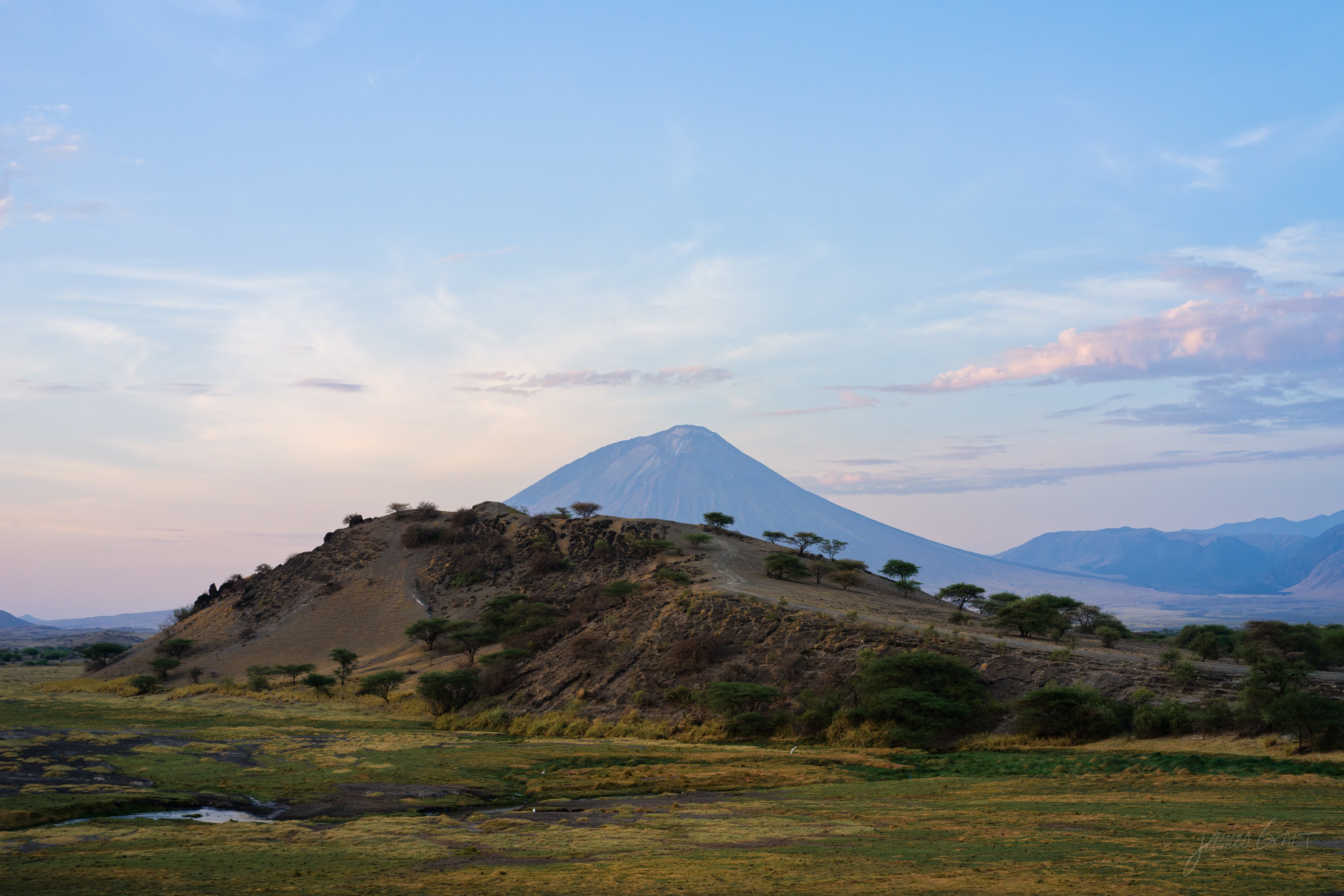 A hazy mountain ridge catching the first warm light of the day above a dark plain, the sky pale gold behind it.