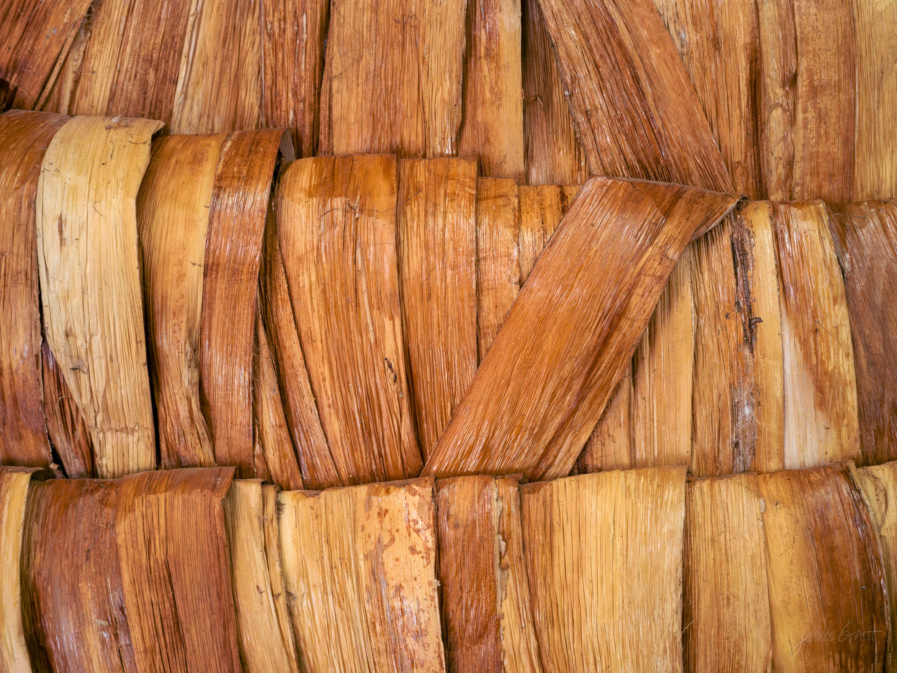 A close view of woven palm-leaf matting, pale strips crossing in a tight over-and-under pattern, warm directional light raking across the surface.