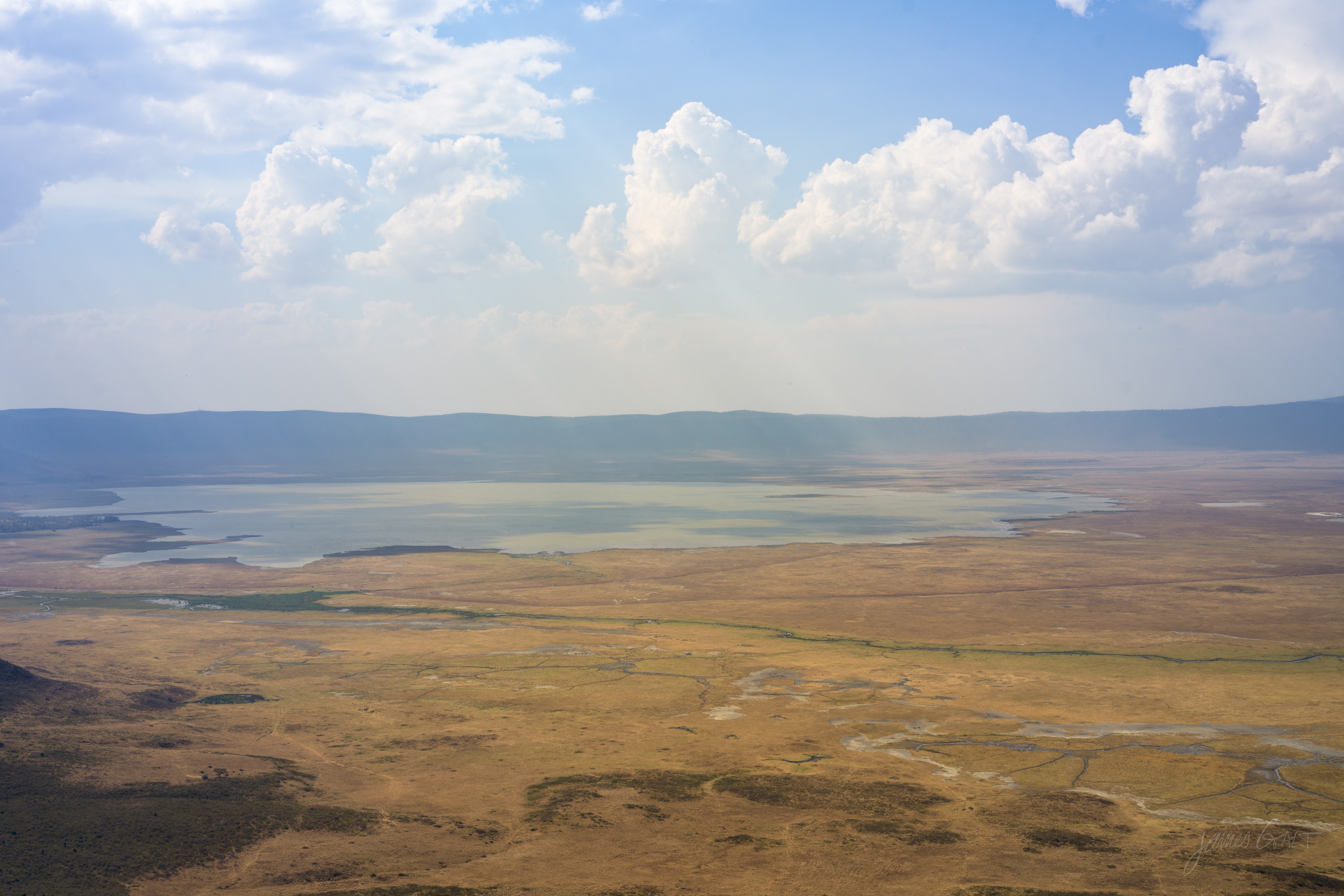 A wide panorama of the Ngorongoro crater, the flat floor stretching to the encircling crater wall in the hazy distance under a high sky.