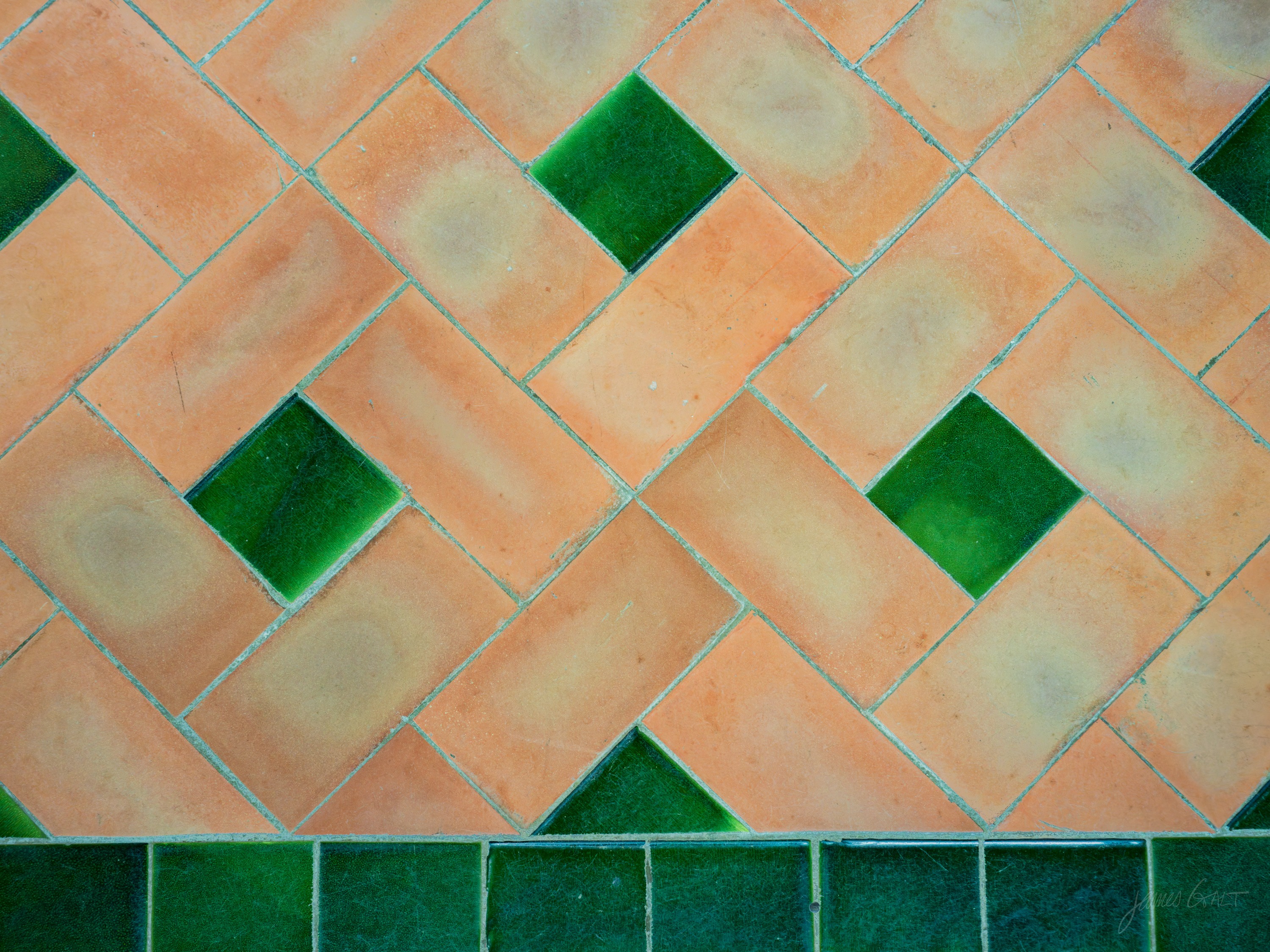 Close view of a floor laid in diagonal terracotta tiles with square green glazed tiles set between them, a band of solid green tile below.