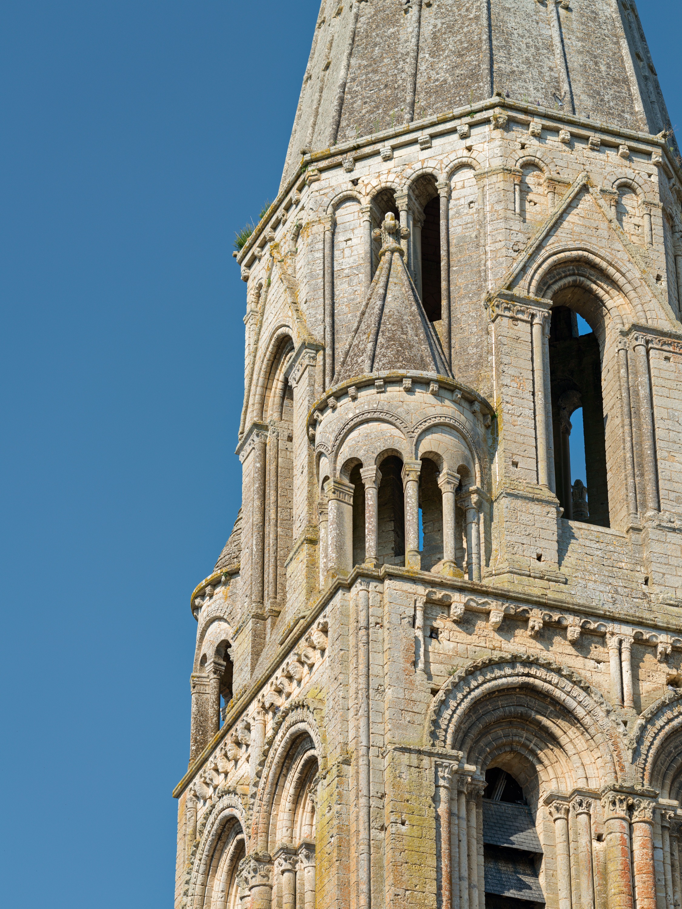 A pale stone Romanesque bell tower with rounded arcaded openings and an octagonal upper stage, against a clear blue sky.