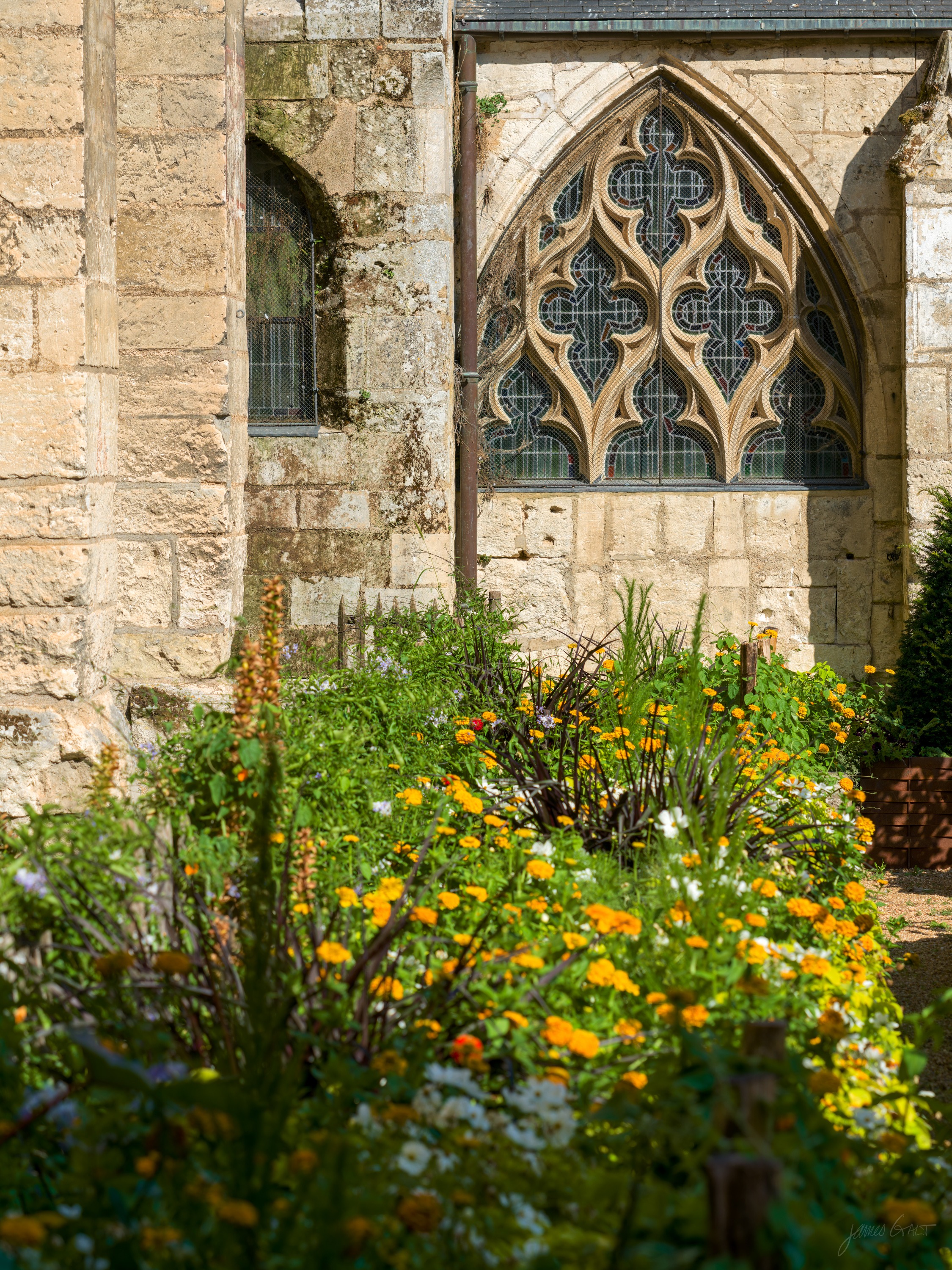 A flamboyant Gothic traceried window above a dense border of orange marigolds and mixed wildflowers.