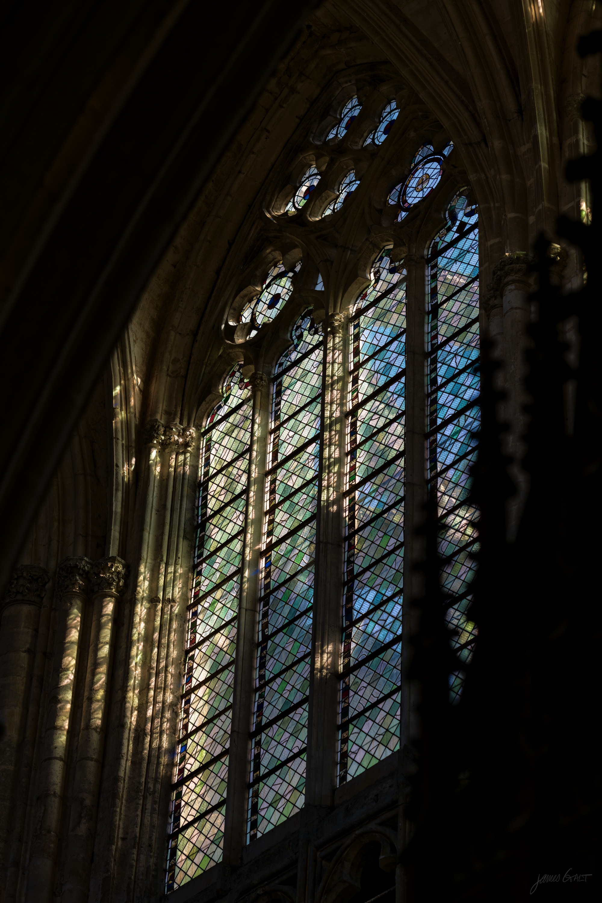 A tall Gothic window in silhouette, its stone tracery dark against bright leaded glass.